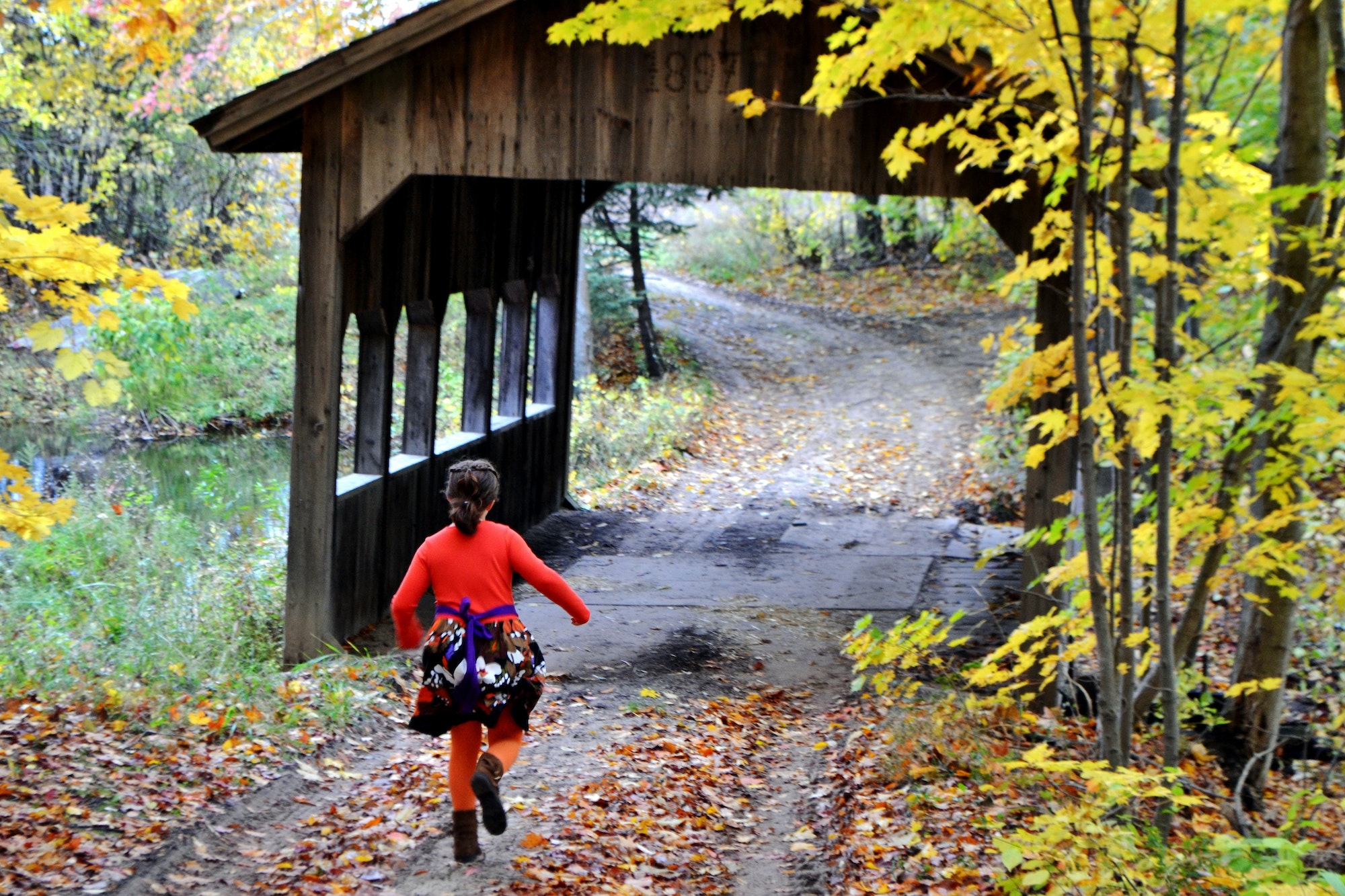 Young girl running towards a wooden covered bridge in the Fall